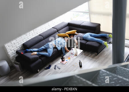 Amici ubriaco che dorme sul divano in camera disordinato After Party Foto Stock