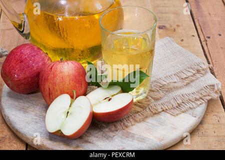 Le mele rosse e il succo di mela in un bicchiere e brocca su un vassoio in legno Foto Stock