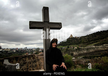 La donna georgiana è seduta accanto alla croce ortodossa sulla collina di Tbilisi, Georgia. Foto Stock