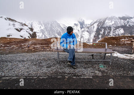 Uomo georgiano seduto su un dosso dietro la vista delle montagne. Autostrada militare georgiana. Georgia. Foto Stock