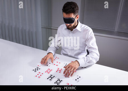 Gli occhi bendati imprenditore della lettura di carte sulla scrivania bianca Foto Stock