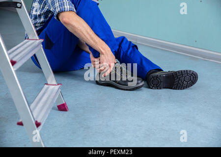 Tuttofare di toccare la sua gamba ferita dopo la caduta dalla scaletta Foto Stock