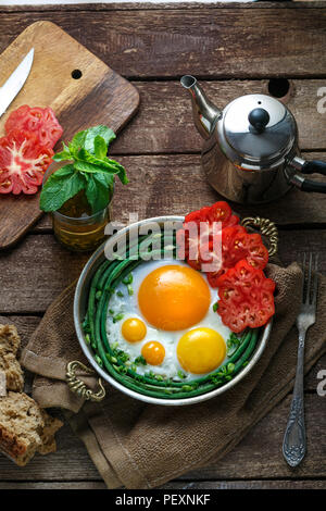 Sunny Side uova fritte in una padella di rame con pomodori e fagiolini, copia dello spazio. Foto Stock