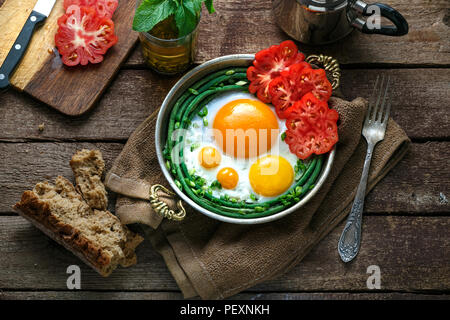 Sunny Side uova fritte in una padella di rame con pomodori e fagiolini, copia dello spazio. Foto Stock