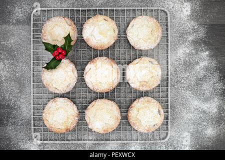 Appena sfornato trito di Natale la torta su un vassoio da forno con agrifoglio e bacche di foglie di ciuffo con zucchero a velo spolvero su legno rustico sfondo Foto Stock