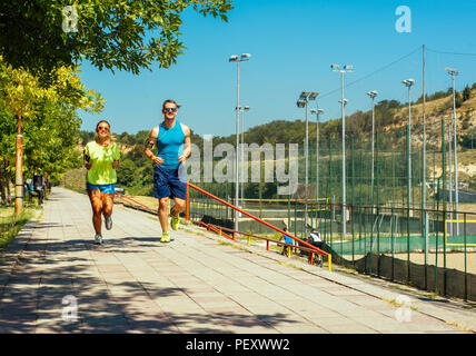 Colpo di giovane donna e uomo che corre attraverso il riverside via Foto Stock