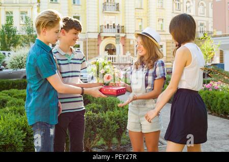 Gruppo di felice amici adolescenti congratularmi con loro fidanzata il giorno del suo compleanno, dare fiori e dono all'esterno. Amicizia e concetto di persone Foto Stock