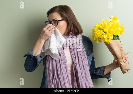La molla allergia ai pollini. Donna con bouquet di fiori gialli sta per starnutire. Sfondo verde parete opaca Foto Stock