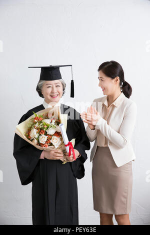 Felice anziani donna che indossa la laurea robe tenendo un bouquet celebrazione con sua figlia. 045 Foto Stock