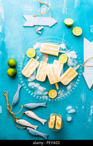 Mango popsicles su una lastra di vetro con cubetti di ghiaccio, intorno artigianale di pesci di legno e un cartello in legno con il testo bech, estate concetto. Foto Stock