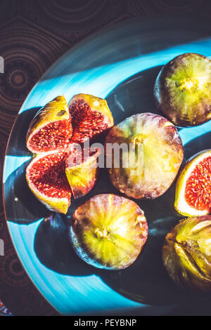 Intero e mezzo taglio fichi maturi sulla piastra blu; sullo sfondo di frutta Foto Stock