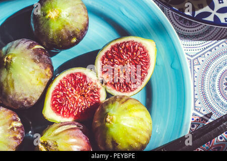 Intero e mezzo taglio fichi maturi sulla piastra blu; sullo sfondo di frutta Foto Stock