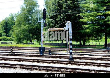 Vecchia ferrovia in metallo bianco e nero della pompa acqua vicino alla ferrovia e il traffico luce montata su un forte polo di metallo e circondato con ghiaia, tracce Foto Stock