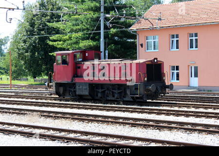 Utilizzate il vecchio rosso scuro locomotiva elettrica in attesa di partenza su binari ferroviari nella parte anteriore della nuova stazione ferroviaria edificio con mazzetto di fili sopra e t Foto Stock