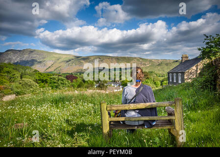 Una giovane donna si siede da solo su una panchina ammirando la vista delle colline di Wasdale, Cumbria, Lake District. Foto Stock