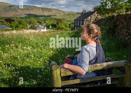 Un attraente donna di mezza età seduto su una panchina di sole godendo di viste di Wasdale, Cumbria, Parco Nazionale del Distretto dei Laghi. Foto Stock