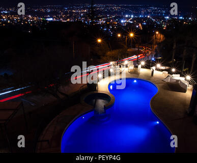 Piscina di notte con le luci della città in background e sentieri di auto in strada Foto Stock