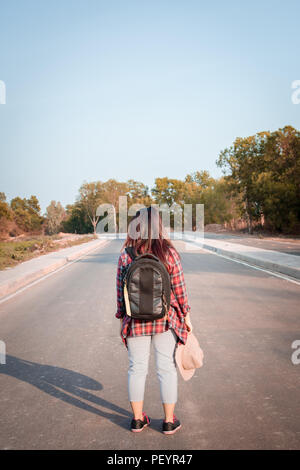 Concetto di viaggio. Donna in viaggio con zaino camminando sulla strada asfaltata campagna Foto Stock