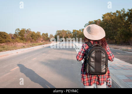 Concetto di viaggio. Donna in viaggio con zaino camminando sulla strada asfaltata campagna Foto Stock