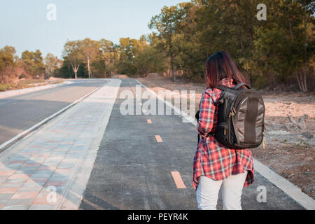 Concetto di viaggio. Donna in viaggio con zaino camminando sulla strada asfaltata campagna Foto Stock