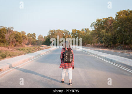 Concetto di viaggio. Donna in viaggio con zaino camminando sulla strada asfaltata campagna Foto Stock