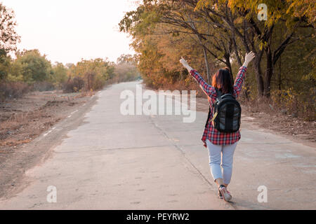 Concetto di viaggio. Donna in viaggio con zaino camminando sulla strada asfaltata campagna Foto Stock