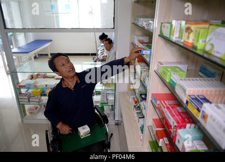 Pechino, Cina. Il 18 agosto 2018. Medico Sun Qingyong (R) recupera la medicina per un paziente presso la clinica di Shaluo villaggio di Guanghuojie township di Ningshan County, Ankang, Cina nord-occidentale della provincia di Shaanxi, 15 agosto 2018. Sole divenne paraplegico in un incidente di traffico 22 anni fa. Presto ha iniziato ad offrire cure mediche ai suoi compaesani su una sedia a rotelle. Credito: Xinhua/Alamy Live News Foto Stock