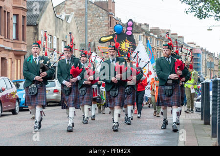 Glasgow, Scotland, Regno Unito. Il 18 agosto, 2018. Il San Francesco Pipe Band leader della parata di Govanhill Festival Internazionale & Carnevale. Quest'anno la sfilata include gruppi di comunità, un pipe band, batteristi, ballerini, giocolieri, rullo pattinatori e una banda di ottoni tutti a partire da Govanhill Park e il viaggio attraverso le strade di Govanhill finendo al Queen's Park Arena. Credito: Berretto Alamy/Live News Foto Stock