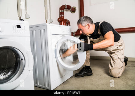 Plumber in riparazioni uniforme all'interno della macchina lavatrice in servizio lavanderia Foto Stock