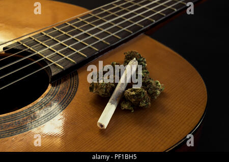 Fretboard ed il corpo di una classica o chitarra spagnola con la marijuana gemme e giunto su di esso. Sfondo nero con effetto di sfocatura. Vista ravvicinata. Foto Stock
