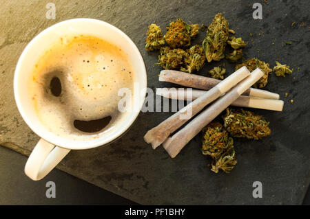 Una deliziosa tazza di caffè, un mucchio di alta qualità boccioli di marijuana con alcuni sigari di erbaccia pronto per il fumo. Vista da sopra con lo sfondo di pietra nera. Foto Stock