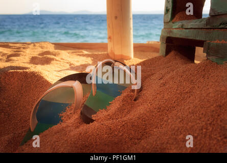 Colorata, il fuoco selettivo flip-flop su una spiaggia di sabbia dorata su una spiaggia in un bar con mobili in legno e soft focus mare Foto Stock
