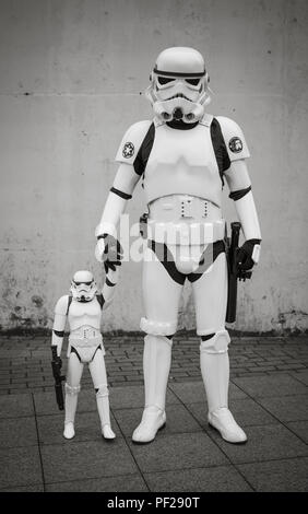 Un maschio cosplayer vestito come un Stormtrooper di Star Wars e tenendo la mano del suo Stormtrooper figlio in un fumetto con ritratto di famiglia Foto Stock