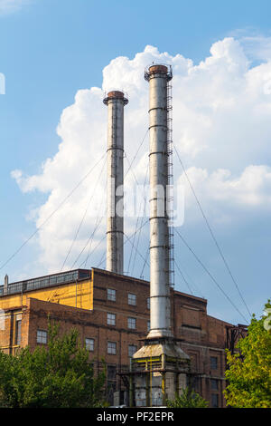 Edificio industriale con due alte ciminiere grigio sullo sfondo azzurro del cielo. Foto Stock