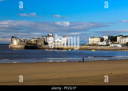 Dog walker su una quasi deserta spiaggia di fronte Knightstone isola in inverno a Weston-super-Mare, North Somerset, Inghilterra, Regno Unito Foto Stock