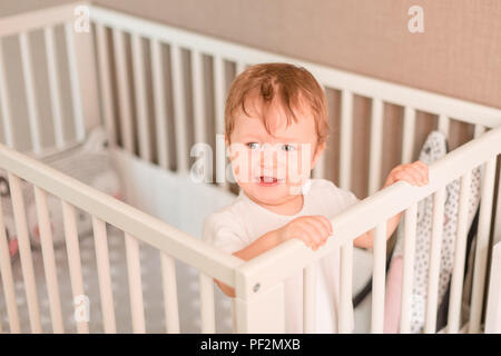 Piccolo Grazioso baby boy guardando fuori del suo letto nella sua camera Foto Stock
