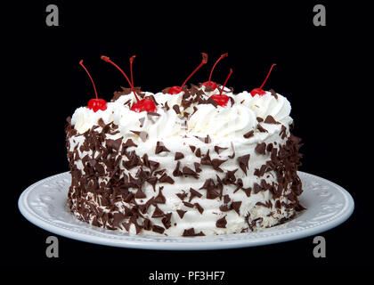 Torta della Foresta nera su una piastra bianca isolata su uno sfondo scuro. Panna montata, rasata caramella di cioccolato, ciliegie sulla parte superiore. Foto Stock