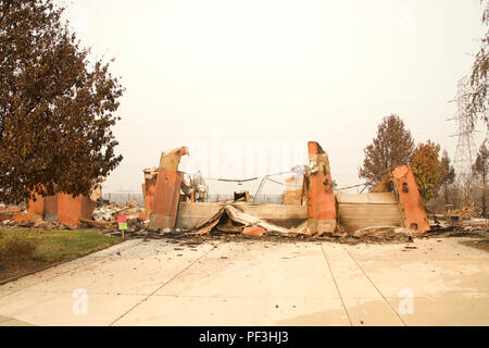 Home rasa al suolo, porta di garage allacciata e la posa di un heap dopo la recente wild fire fire storm in Redding, CA. Fumo e cenere in aria come Foto Stock