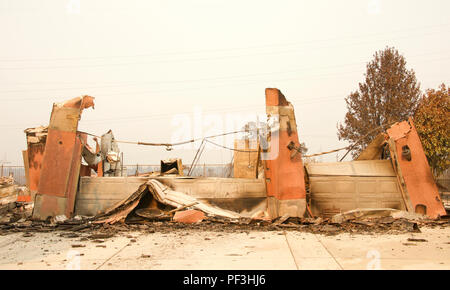 Home rasa al suolo, porta di garage allacciata e la posa di un heap dopo la recente wild fire fire storm in Redding, CA. Fumo e cenere in aria come Foto Stock