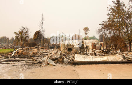 Home rasa al suolo, porta di garage allacciata e la posa di un heap dopo la recente wild fire fire storm in Redding, CA. Fumo e cenere in aria come Foto Stock