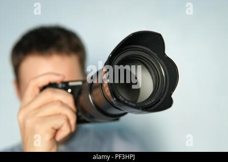 Giovane fotografo su sfondo blu. Fotocamera Mirrorless close up per mano di un giovane uomo su sfondo blu. Il reporter di scattare una foto. Foto Stock