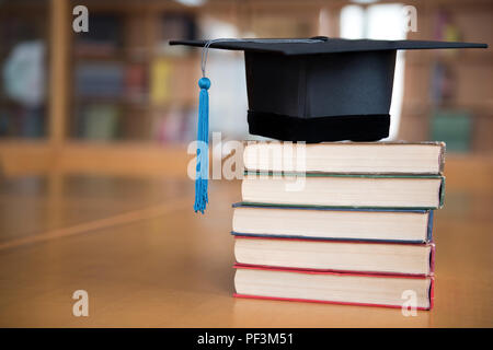 Nero cappuccio graduato e fiocco blu posta sul libro. Foto Stock