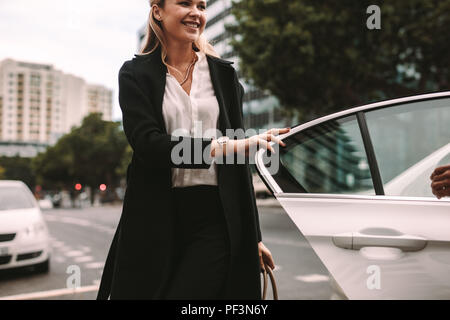 Donna sorridente commuter arrivare al di fuori di un taxi. Imprenditrice scendere una cabina. Foto Stock