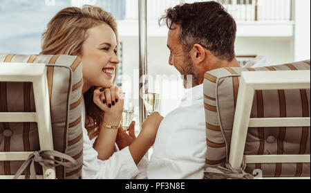 Coppia romantica in accappatoi guardando ogni altro con un bicchiere di vino in mano. Uomo sorridente e donna seduta su sedie a sdraio all'esterno. Foto Stock