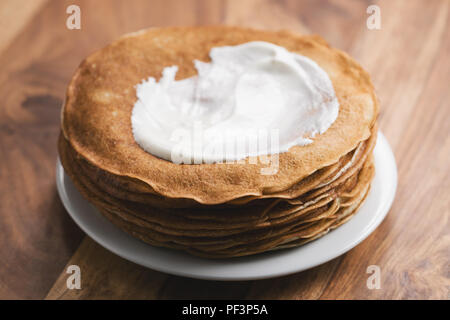 Pila di fresco crepes calda o blinis con panna acida sulla tavola di legno, fuoco poco profonda Foto Stock