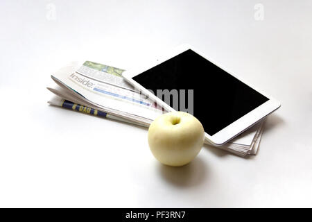 Tavoletta digitale, giornale ripiegato e mela matura su sfondo bianco Foto Stock