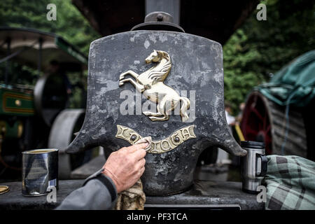 Un appassionato di vapore pulisce la targa sul suo motore di trazione Aveling & Porter mentre dozzine di veicoli alimentati a vapore si riuniscono in un pub a Dorset prima di raggiungere la fiera del vapore Great Dorset, Dove centinaia di motori di trazione a vapore di periodo e attrezzature meccaniche pesanti di tutte le epoche si riuniscono per la mostra annuale dal 23 al 27 agosto 2018, per celebrare i 50 anni. Foto Stock