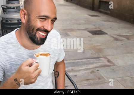 Ritratto di un uomo spagnolo con la barba avente il caffè seduti all'aperto, sorridendo felice, guardando lontano, godimento. Foto Stock
