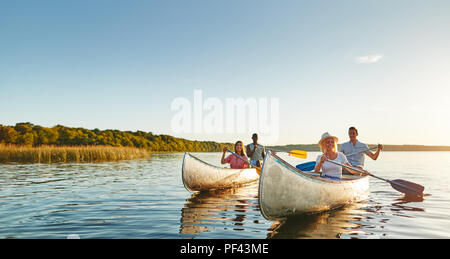 Sorridente due coppie giovani paddling canoe insieme su un lago ancora in un assolato pomeriggio di estate Foto Stock