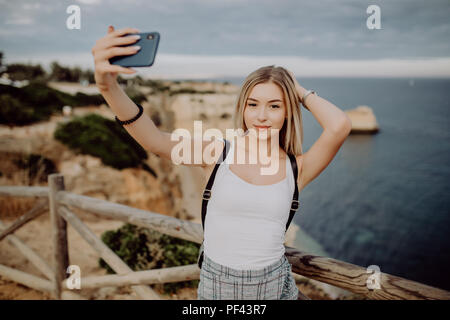 Giovane donna rendendo selfie ritratto sulla costa rocciosa durante il sunrise viaggiare a Lagos il sud del Portogallo Foto Stock